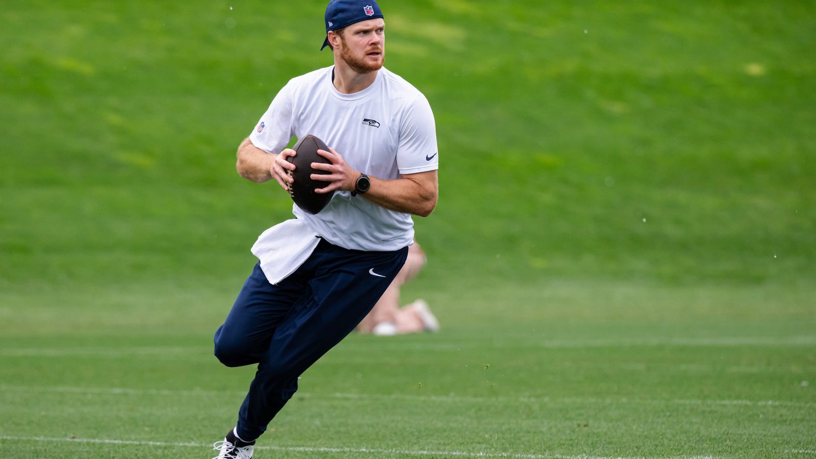 Still from Before the Noise. A Seahawks player carries a football across the field during warmups.