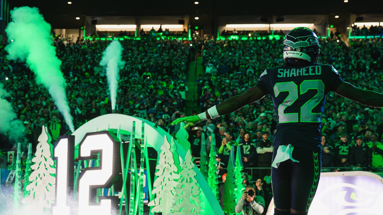 Still from The Specialists. Rashid Shaheed stands with arms outstretched amid green pyrotechnics and smoke during player introductions at Lumen Field.