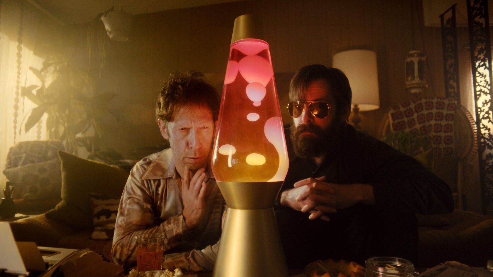 Still from Slugfest: two men lean in toward a glowing red lava lamp in a 1970s living room.