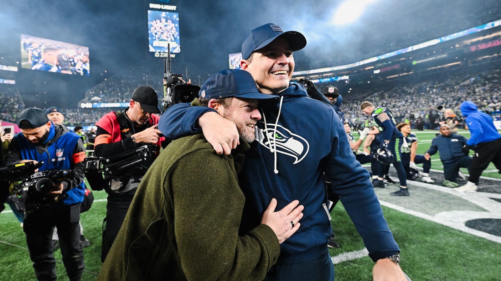 Still from The Sound: Of the Seahawks. Two men embrace on the sideline after a game while camera operators work around them.