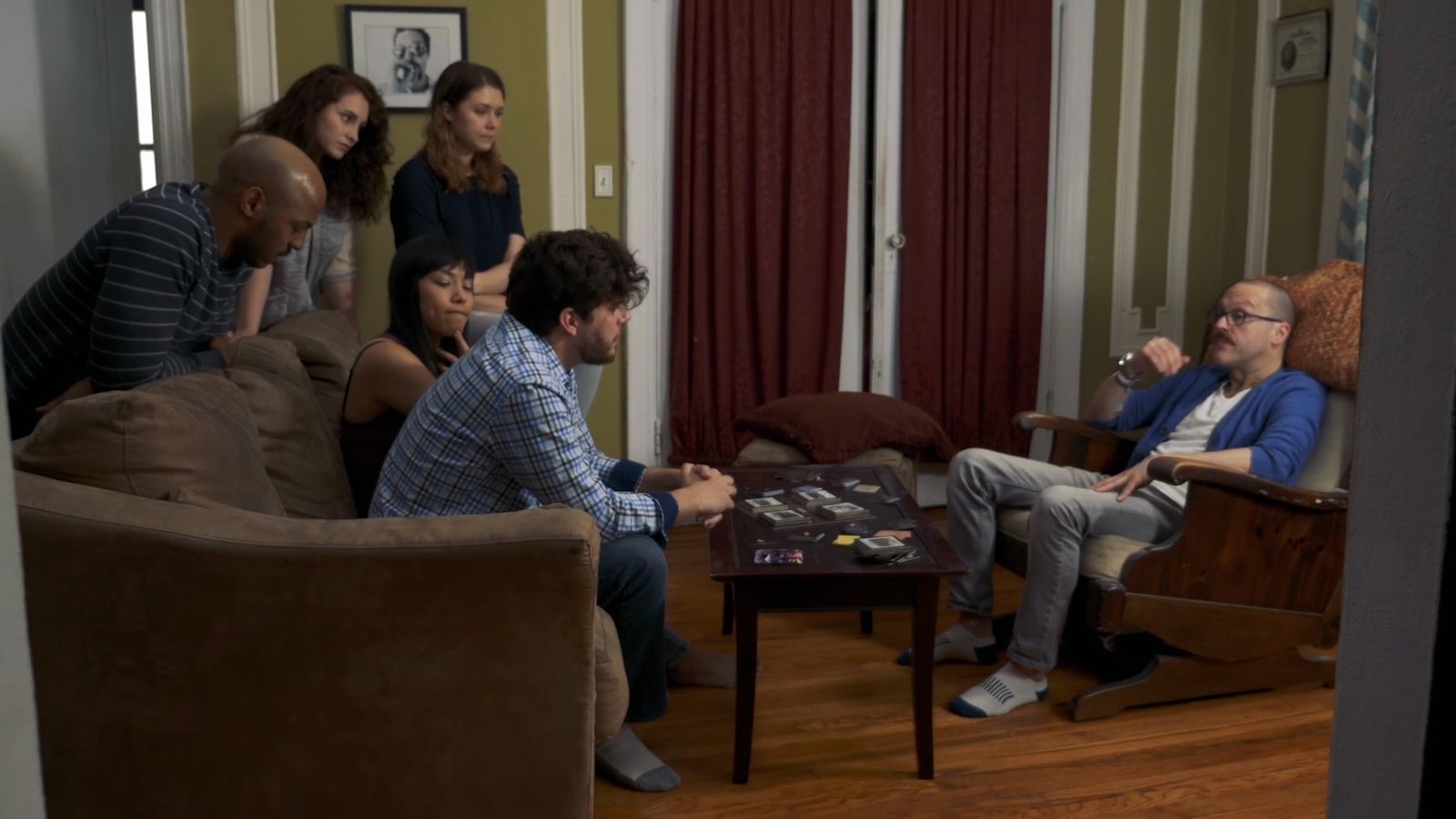 Still from TableTalk: friends gathered around a board game in a living room, one leaning back in an armchair.